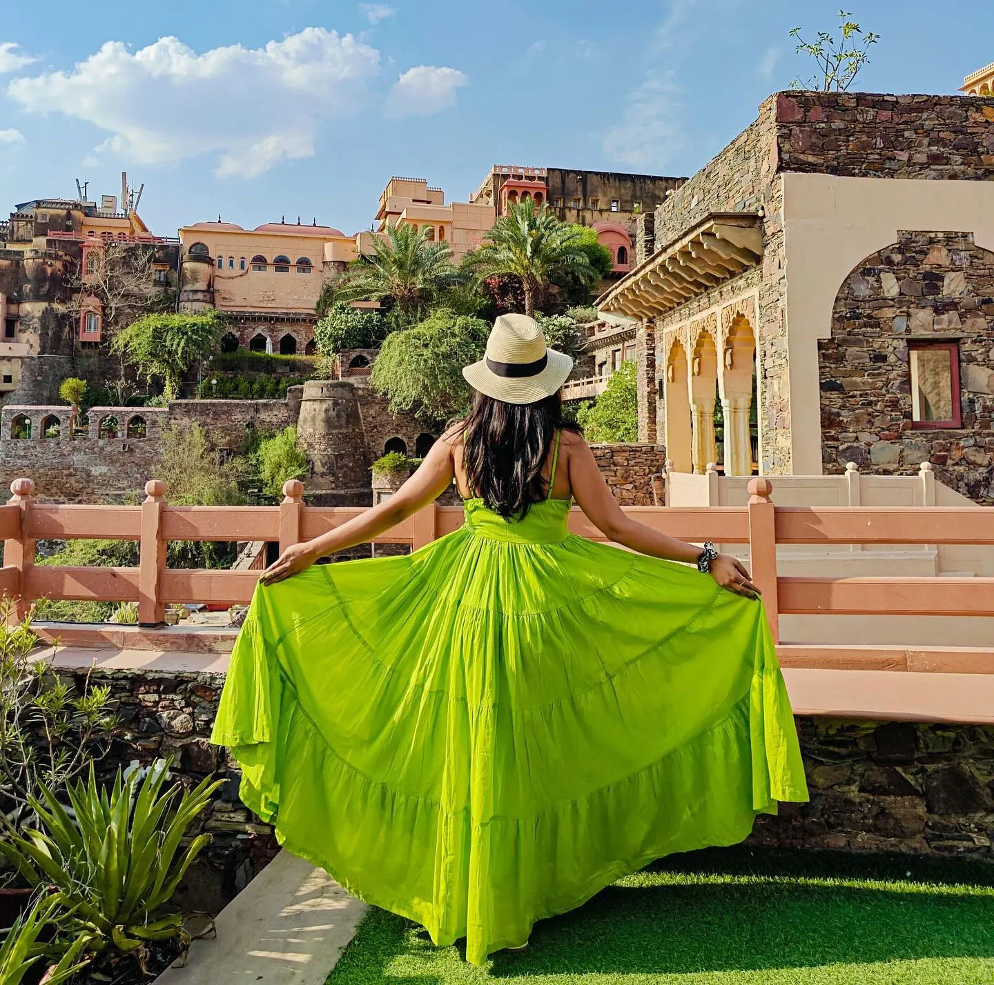 Woman in a green flowing dress enjoying the scenic beauty of a historic Rajasthan heritage fort surrounded by royal architecture and gardens